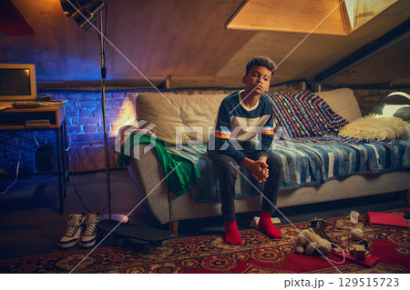 Teen boy sits on couch in cozy retro attic Teen boy sits on couch in cozy retro attic 129515723