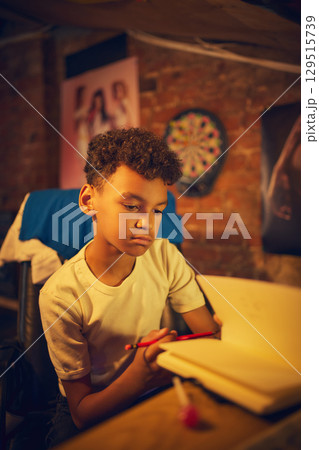 Boy looking down at notebook while holding pencil Boy looking down at notebook while holding pencil 129515739