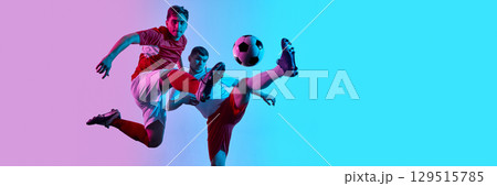 Soccer players in dynamic mid-air kick under pink and blue neon lights. Banner 129515785