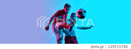 Dynamic soccer action between two players in vibrant blue and purple lighting with ball mid-air. Banner Dynamic soccer action between two players in vibrant blue and purple lighting with ball mid-air. Banner 129515786