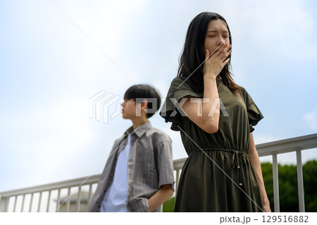 柵にもたれて考え事をする女性と見守る男性 柵にもたれて考え事をする女性と見守る男性 129516882