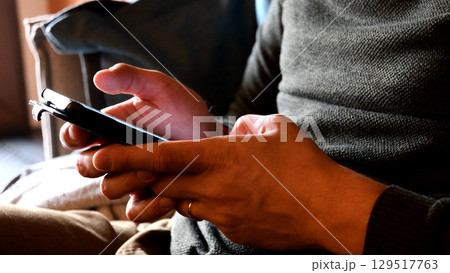 Male hands tapping and swiping his smartphone closeup 129517763