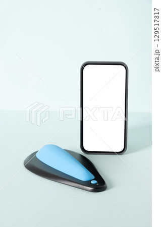 Mens kegel smart trainer and smartphone with empty white blank screen for own apps on beige background. Smart trainer for squeeze pelvic floor muscles with biofeedback and vibration. Modern technology 129517817