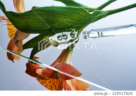 A pipette with a beautiful drop of serum on a background of lily flowers. A pipette with a beautiful drop of serum on a background of lily flowers. 129517820