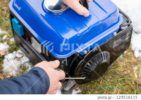 Man turning on the blue generator outdoors, close up. Usage of generator to produce electricity during winter season, blackouts concept 129518115