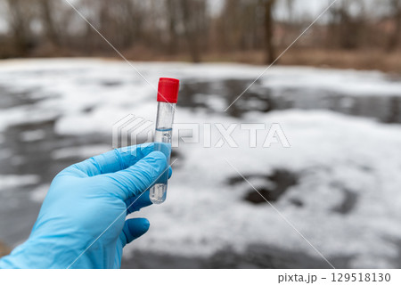 Test tube with water inside in hand of a person, close up. Foam on water surface on the background, checking the pollution level, environmental concept Test tube with water inside in hand of a person, close up. Foam on water surface on the background, checking the pollution level, environmental concept 129518130