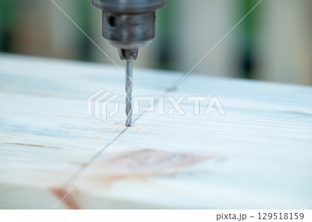 Close up of a drill making a hole for nail or screw in a wooden plank. Handicraft carpentry, drilling a piece of wood to construct something Close up of a drill making a hole for nail or screw in a wooden plank. Handicraft carpentry, drilling a piece of wood to construct something 129518159