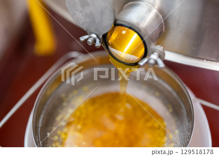 Ripe harvested honey floating from honey extractor through the double cleaning filter. Harvest of honey using professional beekeeping equipment, fresh summer honey 129518178