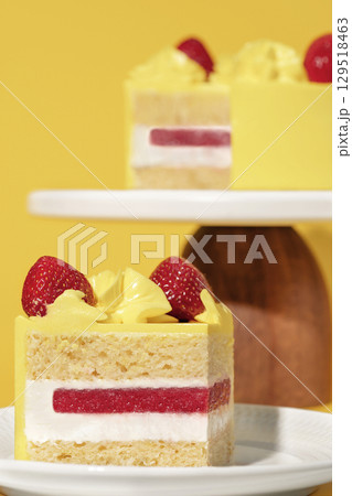 Bento cake featuring layers of lemon sponge and strawberry filling, topped with whipped cream and fresh strawberries, presented on a white plate against a vibrant yellow background Bento cake featuring layers of lemon sponge and strawberry filling, topped with whipped cream and fresh strawberries, presented on a white plate against a vibrant yellow background 129518463