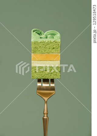 Layered bento cake featuring vibrant mango and passion fruit filling, topped with creamy pistachio frosting, elegantly presented on a golden fork against a soft green backdrop 129518473