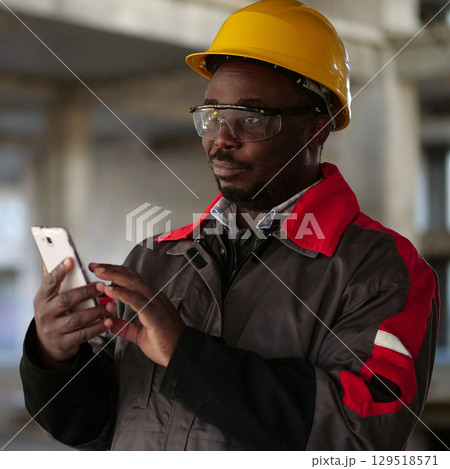 African american workman with smartphone at construction site African american workman with smartphone at construction site 129518571