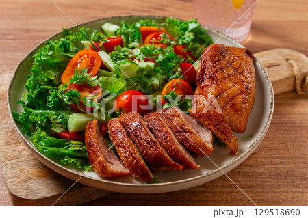 Delicious grilled duck breast served with fresh garden salad and cherry tomatoes at a rustic dining table 129518690