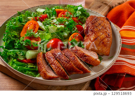Delicious grilled duck breast served with fresh garden salad and cherry tomatoes at a rustic dining table 129518693