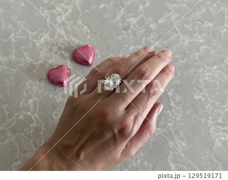 Close up of hand with oval cut diamond ring and pink hearts for Valentine's Day. Close up of hand with oval cut diamond ring and pink hearts for Valentine's Day. 129519171