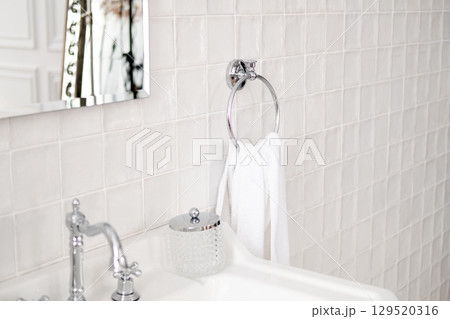 white towel on round iron holder against white tiles and sink with mirror in bathroom 129520316