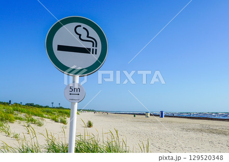 Smoking Area Sign on Sandy Beach with Sea Waves and Dune Grass Under Clear Blue Sky 129520348