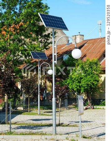 Solar-powered lamp posts in residential courtyard with trees and rustic rooftops on sunny summer day 129520358