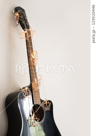 Acoustic guitar decorated Christmas light garland as stars at home. Christmas carols. Xmas holiday celebration. Musical instrument. Acoustic guitar decorated Christmas light garland as stars at home. Christmas carols. Xmas holiday celebration. Musical instrument. 129520446