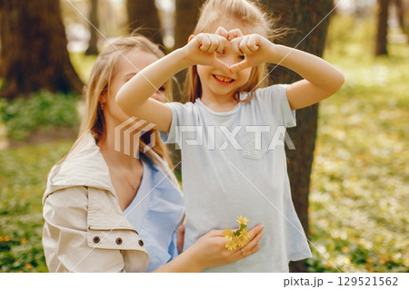 beautiful and elegant young mother with light hair and coat playing with her little cute daughter in a sunny summer park beautiful and elegant young mother with light hair and coat playing with her little cute daughter in a sunny summer park 129521562