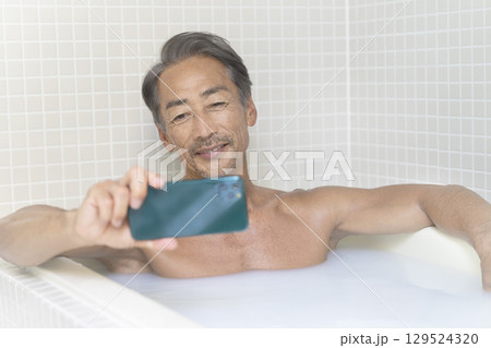 お風呂に入りながらスマホを見るシニア男性 129524320