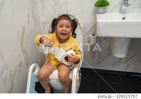 happy toddler girl is sitting on toilet with tissue at home. potty training and learning happy toddler girl is sitting on toilet with tissue at home. potty training and learning 129525787