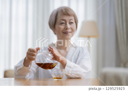 ダイニングでお茶を入れるシニア女性 ダイニングでお茶を入れるシニア女性 129525923