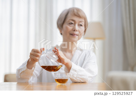 ダイニングでお茶を入れるシニア女性 ダイニングでお茶を入れるシニア女性 129525927