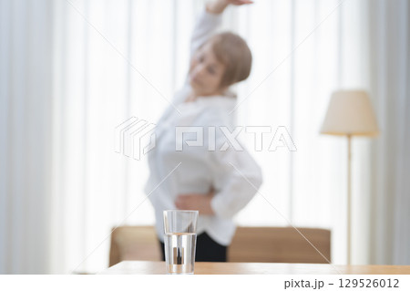 リビングでストレッチをして水を飲むシニア女性 129526012