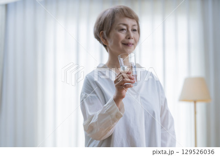 リビングでストレッチをして水を飲むシニア女性 リビングでストレッチをして水を飲むシニア女性 129526036