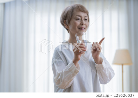 リビングでストレッチをして水を飲むシニア女性 リビングでストレッチをして水を飲むシニア女性 129526037