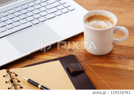 リング式のシステム手帳を広げ、コーヒー（カフェ・ラテ）を飲みながらパソコンでデスクワーク中のイメージ 129528761