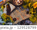 Mystic still life with decorated magic book of spells, tarot card, tansy flowers, crystals, black candles and witchy ritual objects on old table. Occult, esoteric and wicca concept Mystic still life with decorated magic book of spells, tarot card, tansy flowers, crystals, black candles and witchy ritual objects on old table. Occult, esoteric and wicca concept 129528799