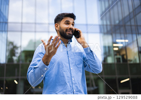 A man with a beard is talking on a cell phone in front of a modern building. 129529088
