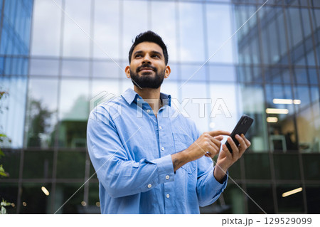 A thoughtful man uses a smartphone outside a modern building. A thoughtful man uses a smartphone outside a modern building. 129529099