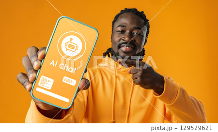 Young man excitedly shows smartphone screen displaying AI chat interface in bright orange setting 129529621