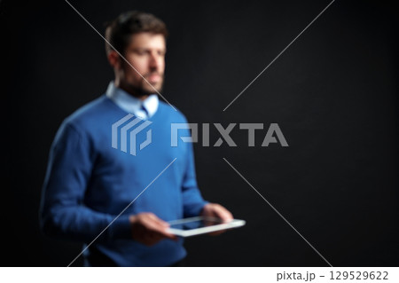 Man in blue sweater holds tablet in dark studio setting during a business presentation session 129529622