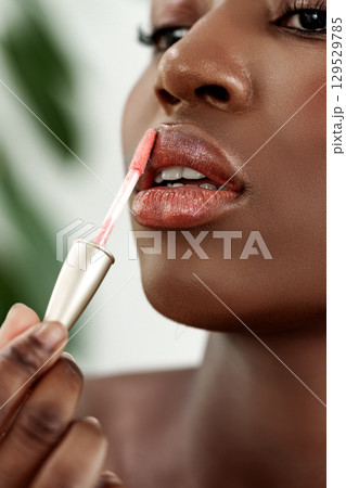 Woman applying lip gloss in a beauty routine at home during the day with plants in the background Woman applying lip gloss in a beauty routine at home during the day with plants in the background 129529785