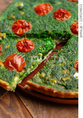Delicious savory spinach tart with cherry tomatoes served on a wooden plate at a cozy kitchen setting 129529812