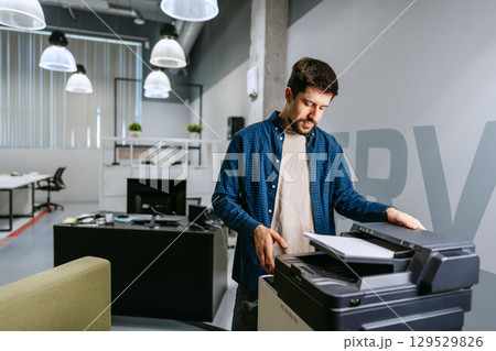 Man operating a printer in a modern office environment during working hours Man operating a printer in a modern office environment during working hours 129529826