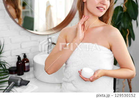 Woman applying skincare cream in a modern bathroom with fresh decor during morning routine 129530152