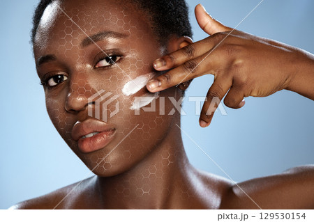 Woman applying skincare product on her face against a blue background showcasing a honeycomb pattern Woman applying skincare product on her face against a blue background showcasing a honeycomb pattern 129530154