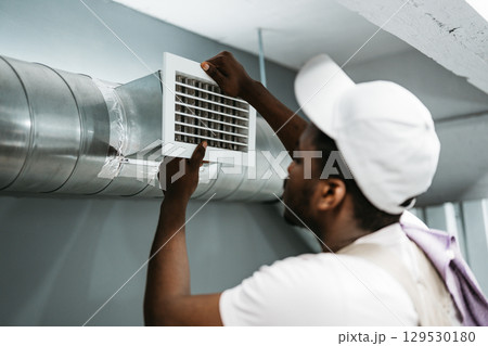 Worker installing air duct vent in a residential basement during the day 129530180