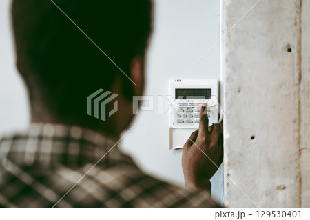 Man setting security system at home in the afternoon, focusing on keypad and monitoring device for safety 129530401