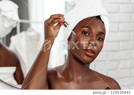Woman applying facial serum in a bright bathroom while preparing her skincare routine Woman applying facial serum in a bright bathroom while preparing her skincare routine 129530445