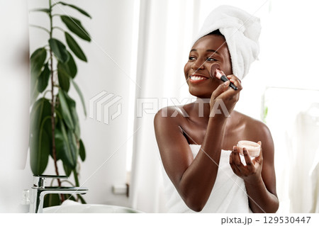 Woman applying skincare product in bright bathroom with greenery in the background 129530447