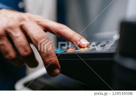 Hand pressing buttons on a multifunction printer in an office environment during work hours 129530506