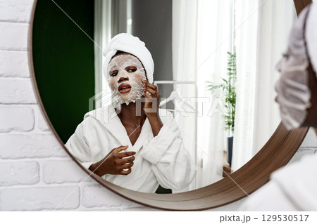 Self-care routine in a bright bathroom with a woman applying a facial mask and wearing a robe Self-care routine in a bright bathroom with a woman applying a facial mask and wearing a robe 129530517