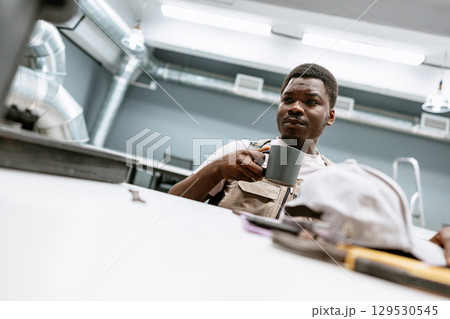 Man enjoying coffee in a workshop setting while taking a break from his tasks 129530545