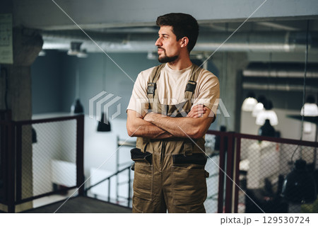 Workplace setting featuring a man in overalls reflecting on his tasks in an industrial environment during daytime Workplace setting featuring a man in overalls reflecting on his tasks in an industrial environment during daytime 129530724