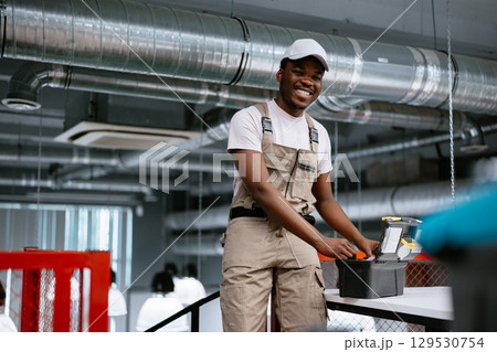 Skilled worker in a modern workspace smiles confidently while organizing tools during industrial setup 129530754